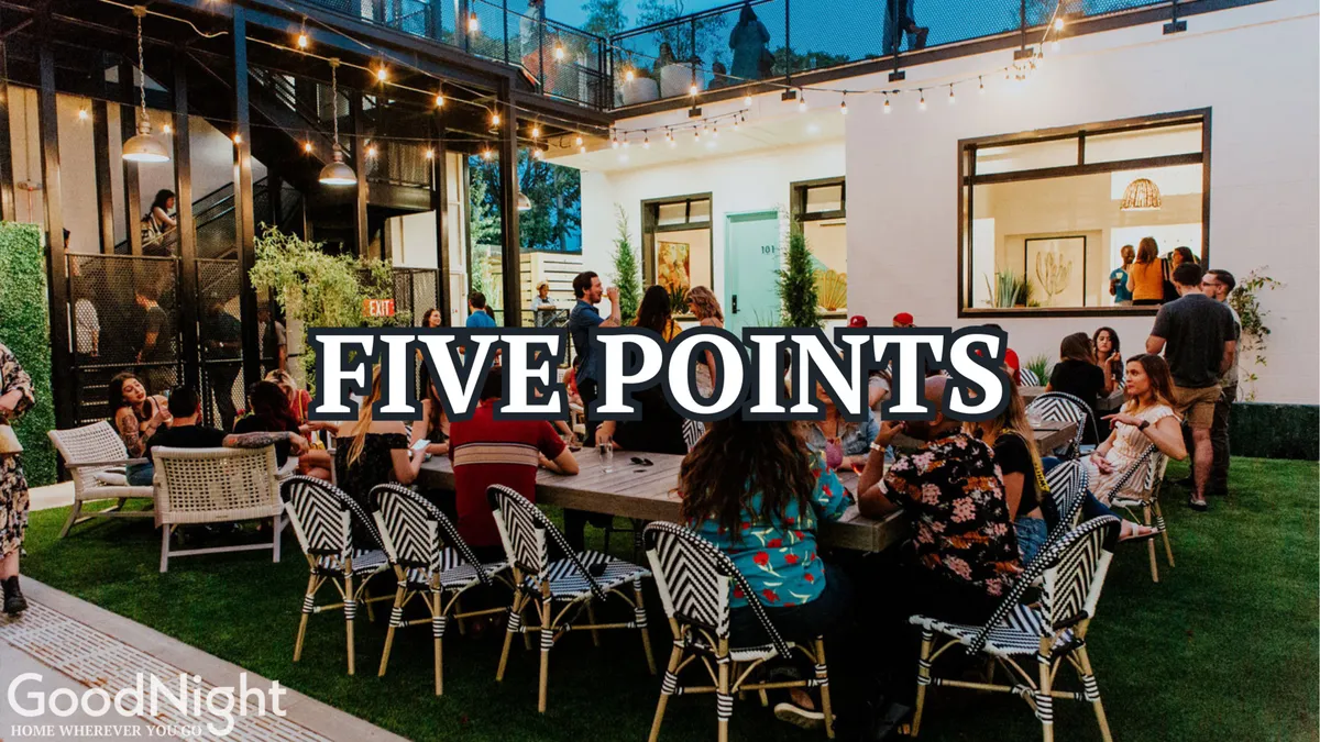 An inviting outdoor scene featuring a large group of people gathered around a table under glowing string lights, with modern architecture providing a stylish backdrop. The communal atmosphere suggests celebration, shared meals, and meaningful social connections.