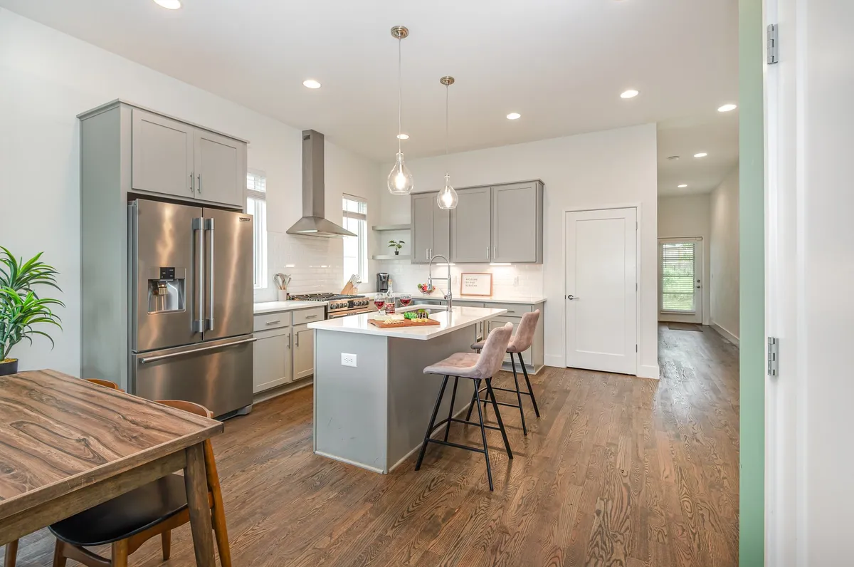 A spacious, modern kitchen featuring a large kitchen island with bar stools, a stainless steel refrigerator, and a wooden dining table. The space is open and inviting, perfect for both meal prep and social gatherings.