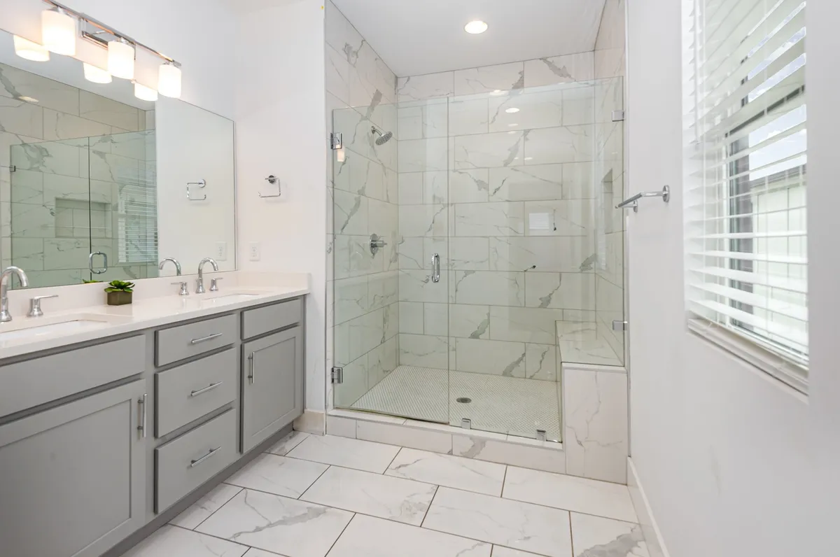 A serene bathroom with a double sink vanity, a glass shower enclosure, and marble tile accents. The space is bathed in natural light and has a calming, spa-like atmosphere, with plenty of counter space for getting ready.