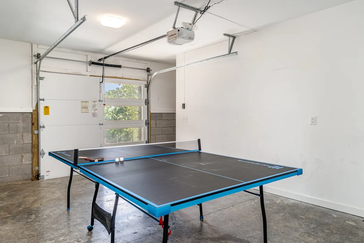 This image captures a garage recreation area equipped with a ping-pong table, concrete flooring, and a large garage door. The setup is ideal for family game nights or friendly competitions, reflecting the playful side of the social hubs described in the section.