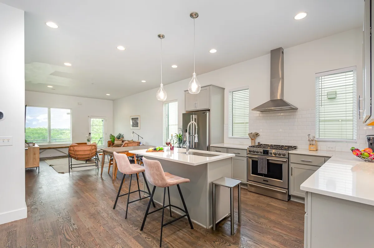 A contemporary kitchen and dining area with a large kitchen island, stainless steel appliances, modern light fixtures, wooden flooring, and a connected dining space. The setting is bright and perfect for hosting, cooking, and enjoying meals together.