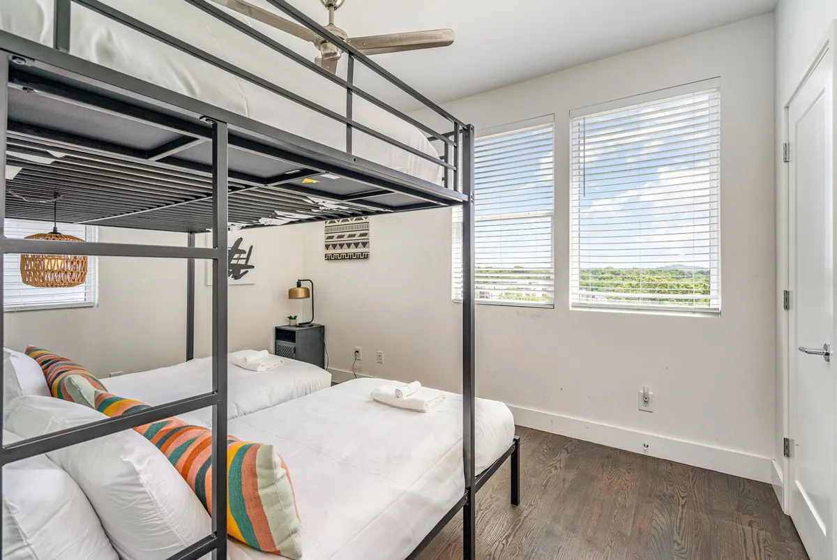 A cheerful bunk room with a sturdy bunk bed, colorful pillows, and large windows allowing plenty of natural light. The playful decor and inviting bedding make it ideal for children or friends traveling together.