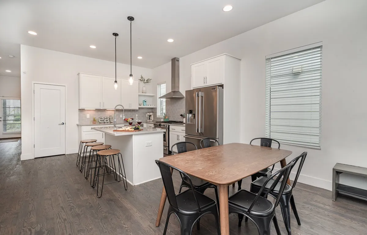 A warm, welcoming kitchen and dining area, equipped with stainless steel appliances, a prominent kitchen island, a wooden dining table, and stylish pendant lights. The space is ideal for family meals and group cooking sessions.